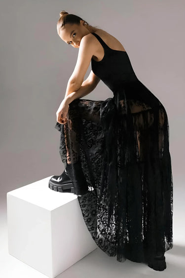 Woman in a black skirt leaning on a white cube against a gray background